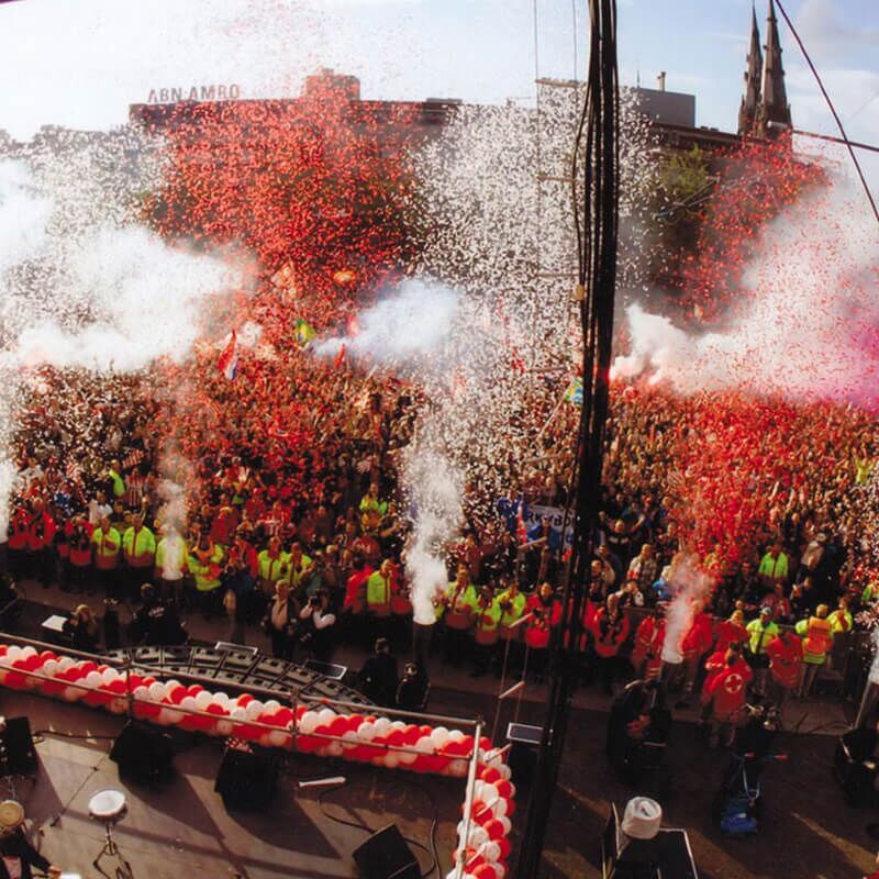 Large outdoor crowd with red and white confetti blasts during a live event