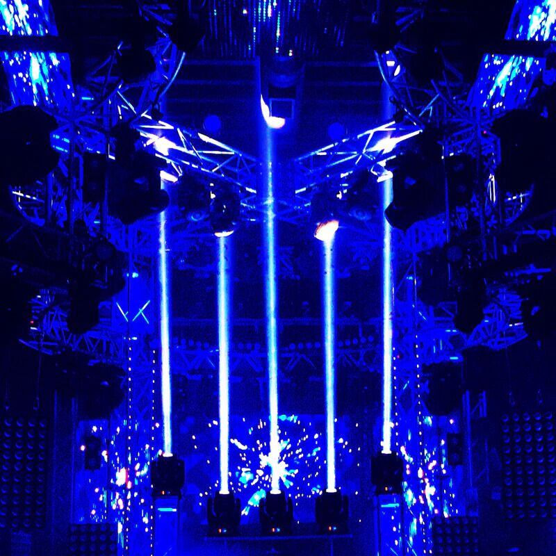 Vizi Beam 5RX fixtures creating intersecting white beams of light on a stage setup with LED screens and trusses